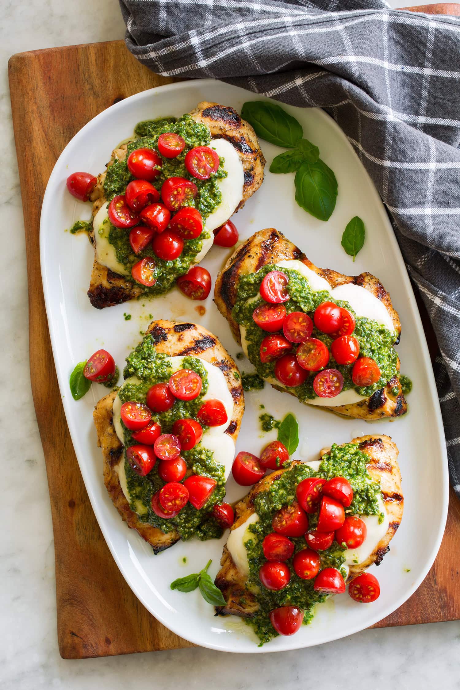 Overhead photo of four pieces of chicken margherita on a white oval serving platter.