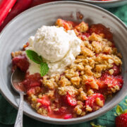 Single serving of strawberry rhubarb crisp shown in a grey bowl with ice cream on top.